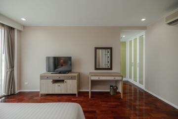 Modern bedroom with wooden flooring, a TV on a stand, a dressing table with a mirror, and a large wardrobe