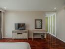 Modern bedroom with wooden flooring, a TV on a stand, a dressing table with a mirror, and a large wardrobe