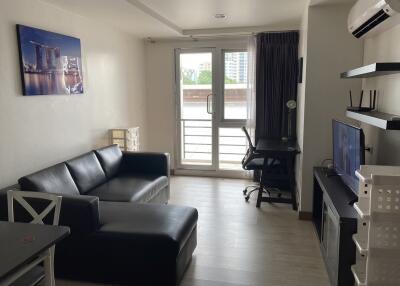 Modern living room with a black leather sofa, air conditioning, and a TV, featuring a cityscape art piece.