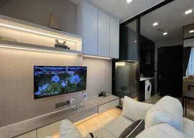 Modern living room with TV, shelves, and view into kitchen area