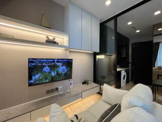 Modern living room with TV, shelves, and view into kitchen area