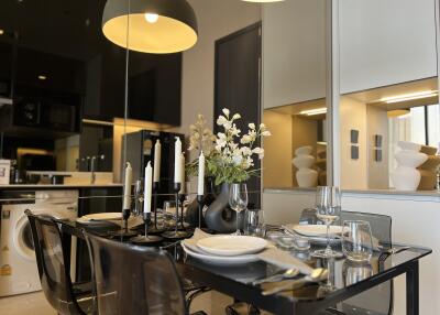 Modern dining area with a reflective glass table, stylish decor, and kitchen background