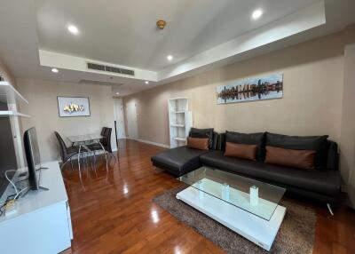 Modern living room with hardwood floors, large black sofa, glass coffee table, dining area, and wall art.