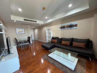 Modern living room with hardwood floors, large black sofa, glass coffee table, dining area, and wall art.