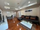 Modern living room with hardwood floors, large black sofa, glass coffee table, dining area, and wall art.