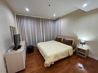 A well-furnished bedroom with a large bed, TV, and bedside table