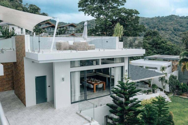 Modern luxury villa exterior with rooftop terrace and glass walls surrounded by lush greenery