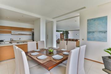 Modern dining area with white chairs, wooden table and a view into the kitchen and living space